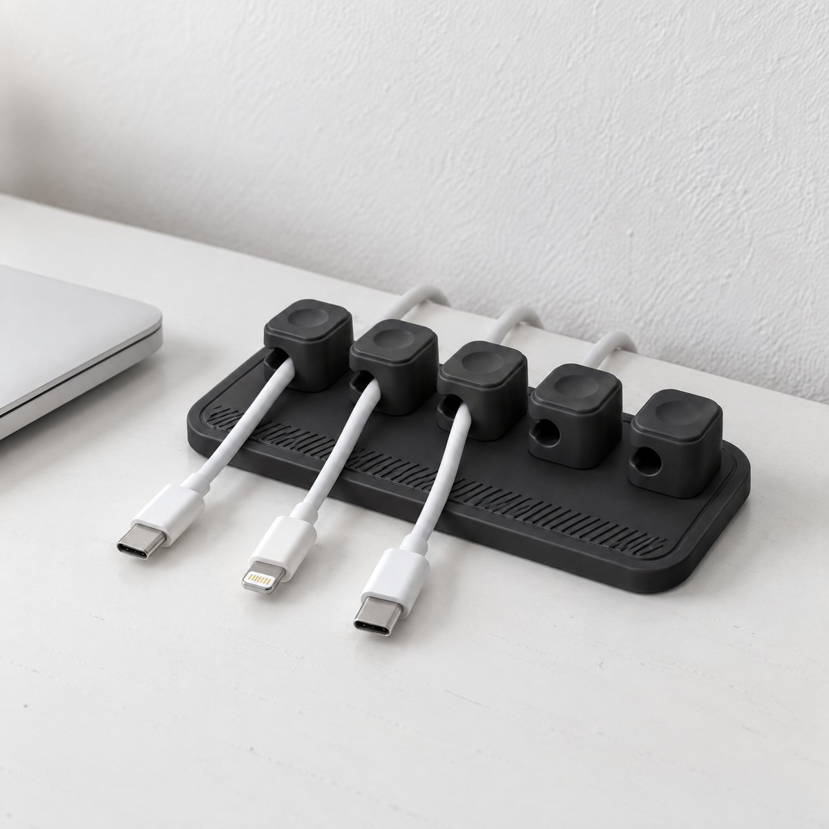 Black magnetic cable holder at the back of a white desk, holding white charging cables