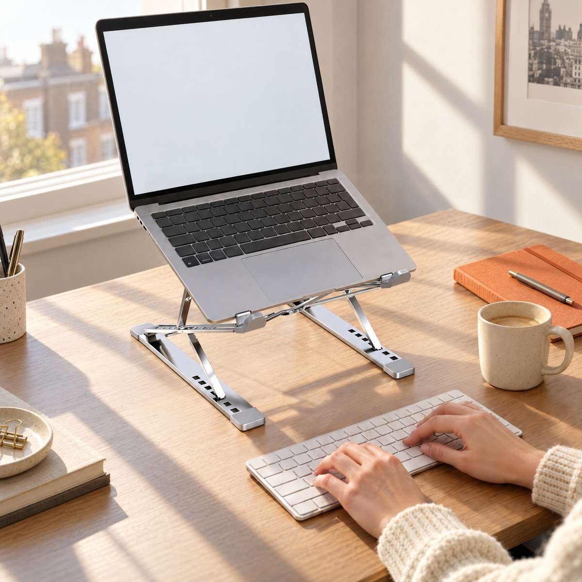 Hands typing on a keyboard in front of a laptop raised on the Tall stand in silver