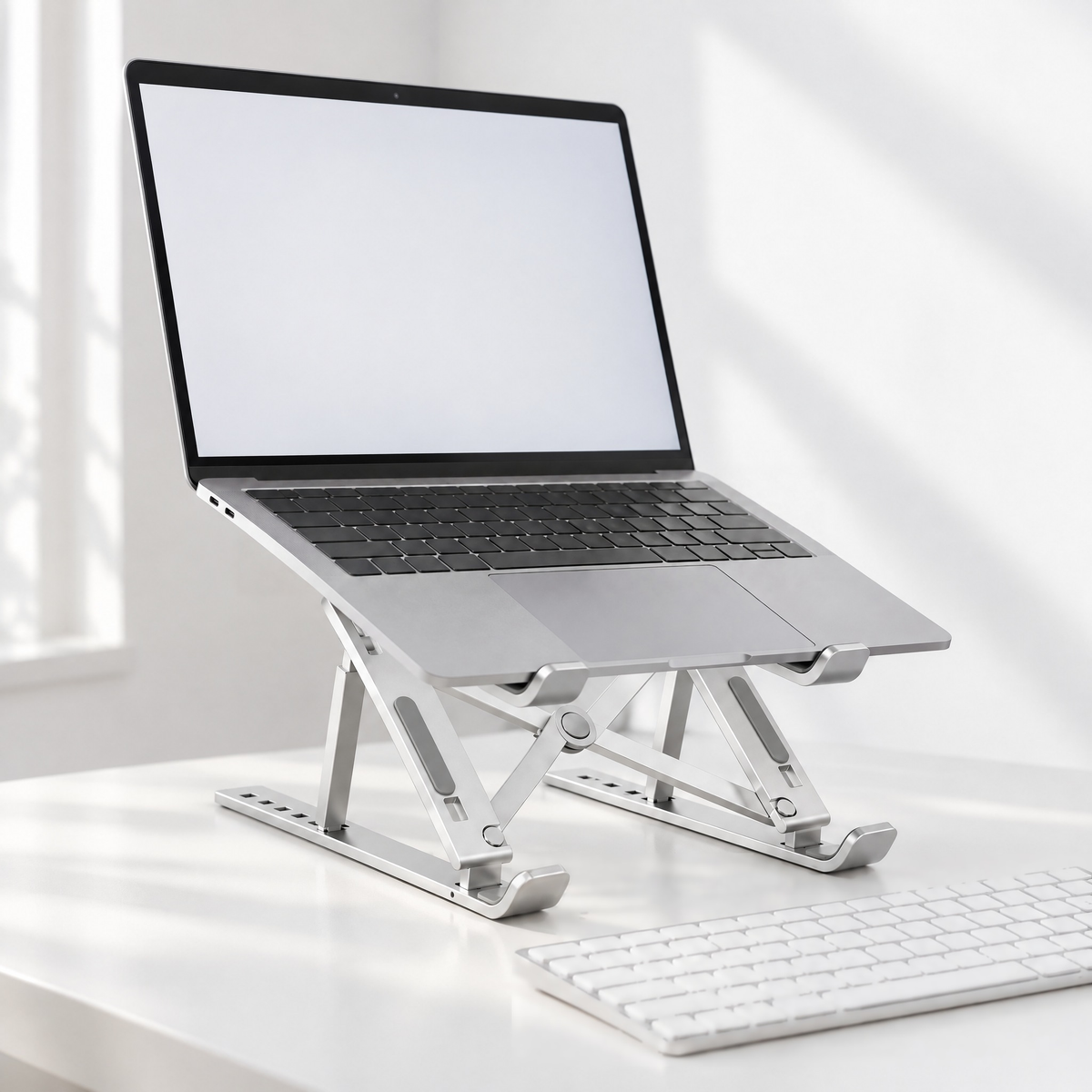 Standard folding aluminium laptop stand in silver holding a laptop on a white desk