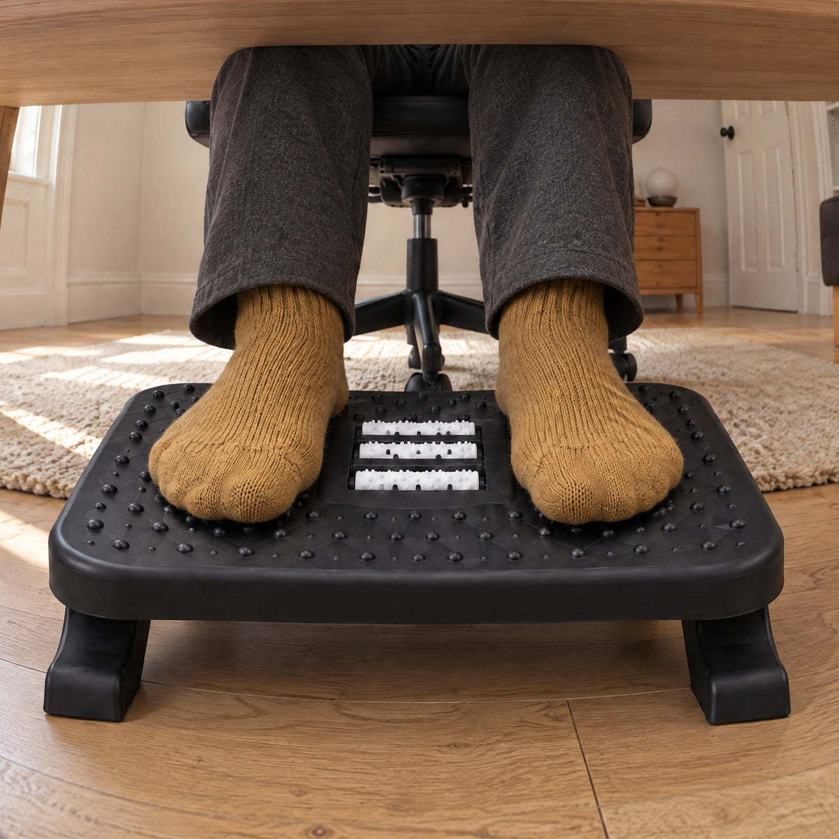 Feet in mustard socks resting on the Ease footrest under a desk, seen from the floor