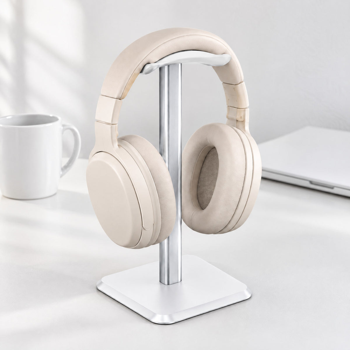 Perch headphone stand in white with a silver upright, holding cream headphones on a white desk