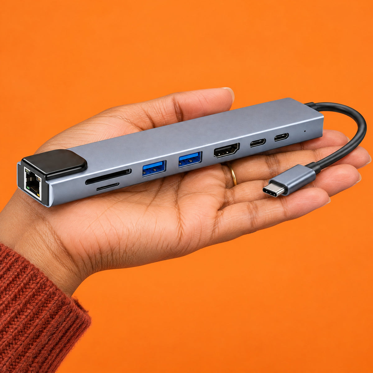 Junction 8-in-1 USB-C hub resting on an open hand against an orange backdrop