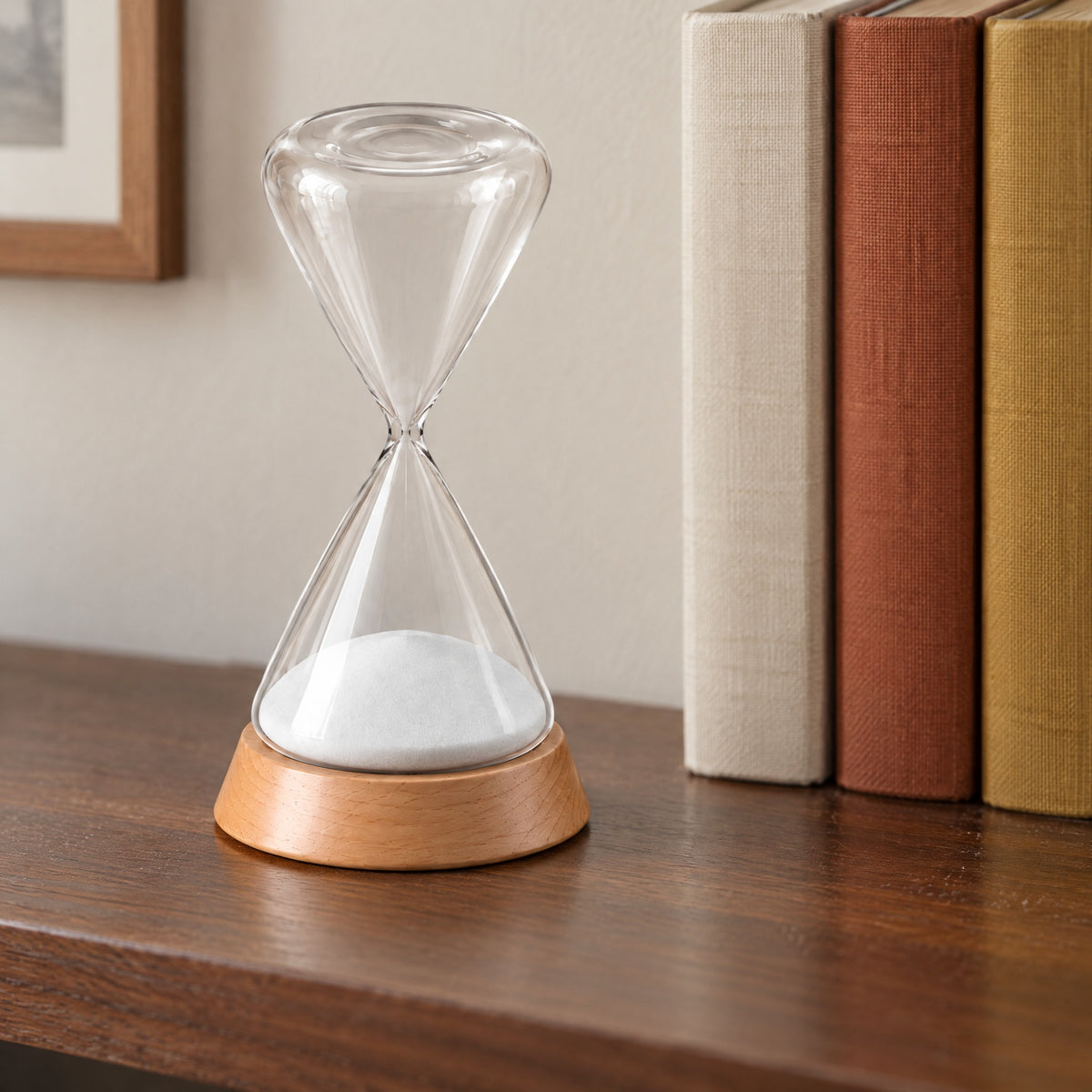 Ebb glass hourglass on a walnut shelf beside cloth-bound books