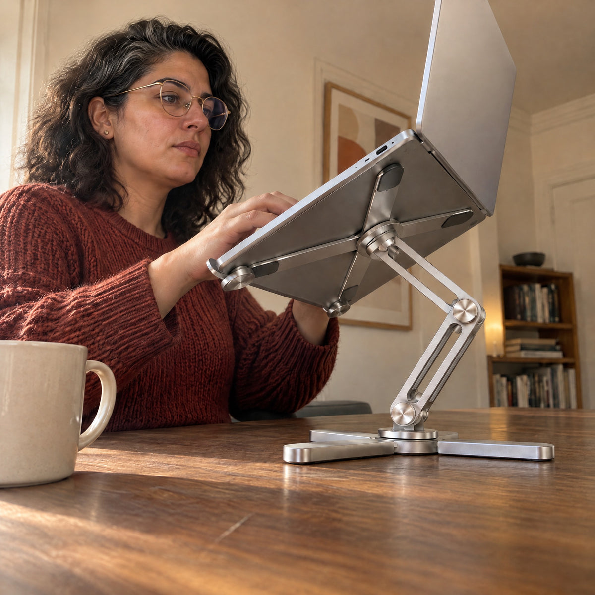 Woman typing on a laptop raised on the silver AeroSpin 360 stand, seen from desk level