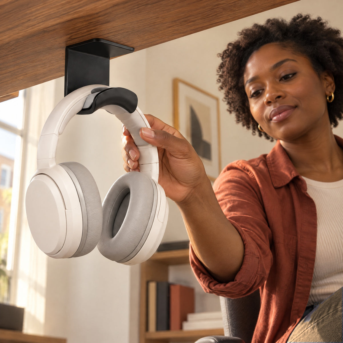 Woman lifting her headphones off the black Eave hook stuck under her walnut desk