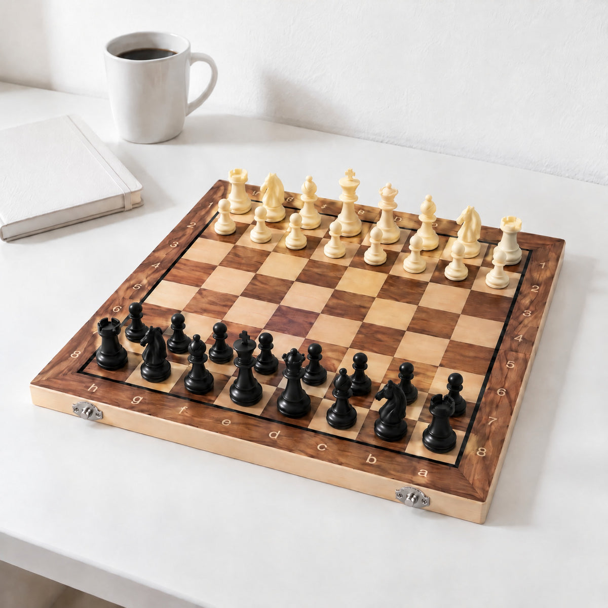 Gambit folding chess set open on a white desk with all 32 pieces in the starting position