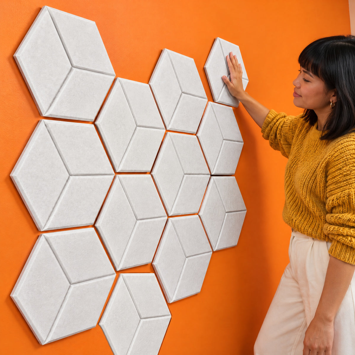 Woman pressing the last white Hive cube acoustic panel into a honeycomb of twelve on an orange wall