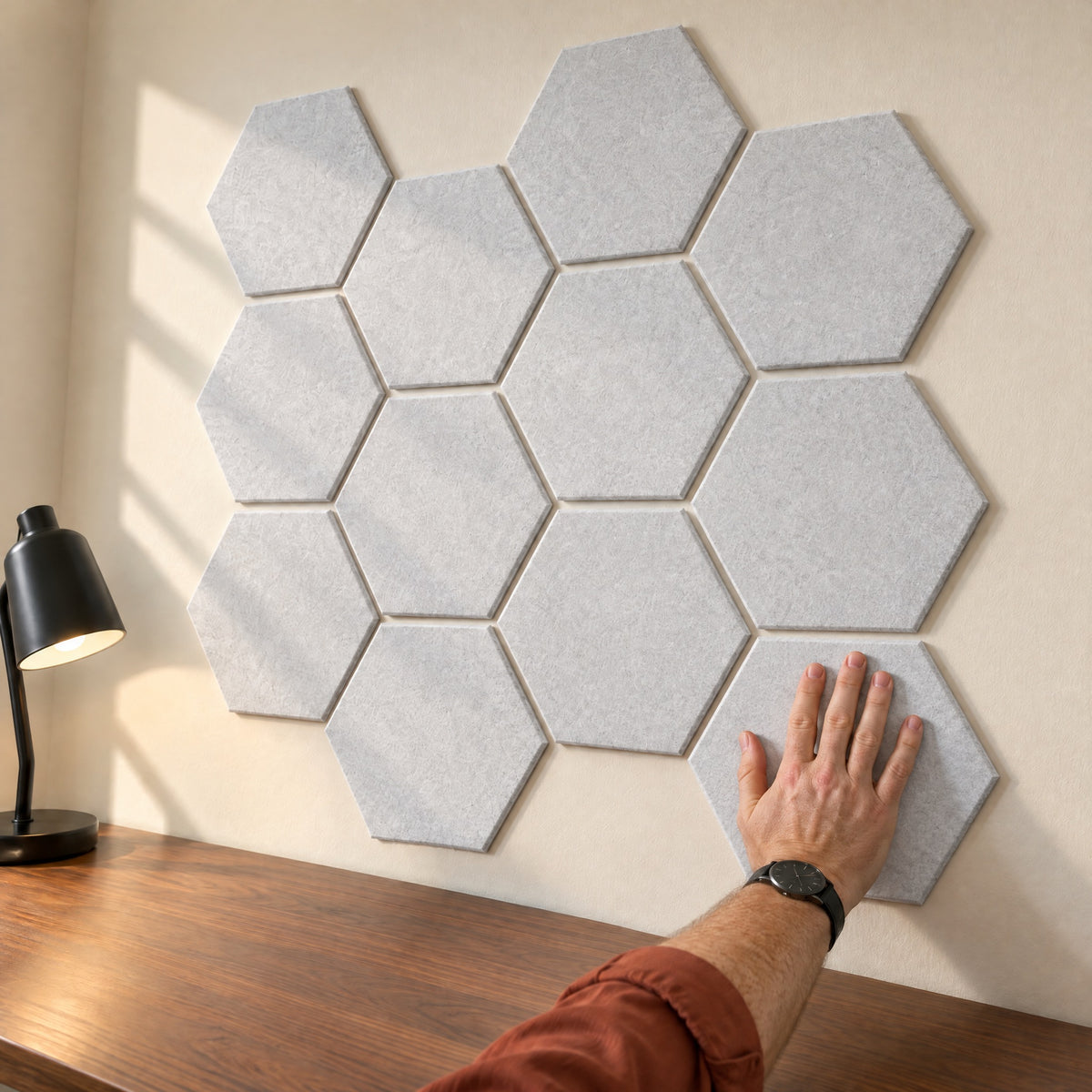 Hand pressing a grey plain Hive hexagon panel onto a cream wall above a walnut desk