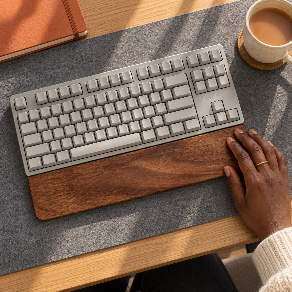 Hand sliding the Sill walnut wrist rest against a grey keyboard on a felt desk mat