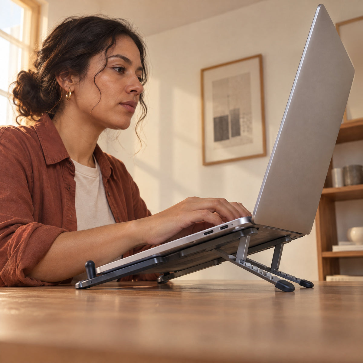 Woman typing on a laptop raised on the Span stand, its front stop holding the laptop's edge