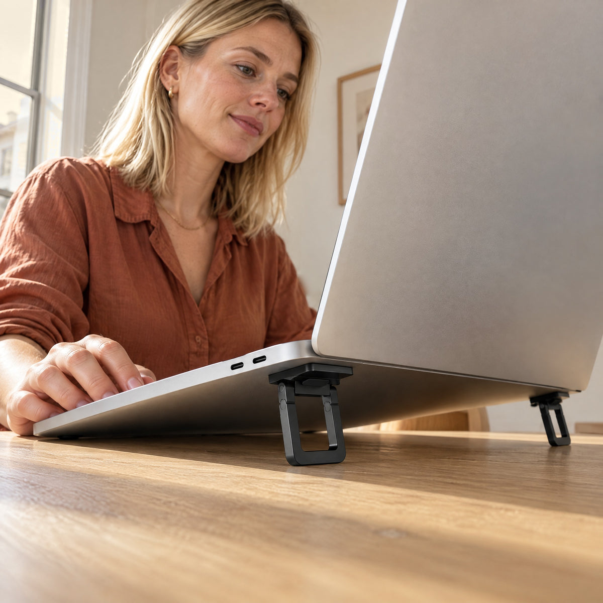 Woman adjusting her laptop, raised at the back on black Stilt folding feet, seen from desk level