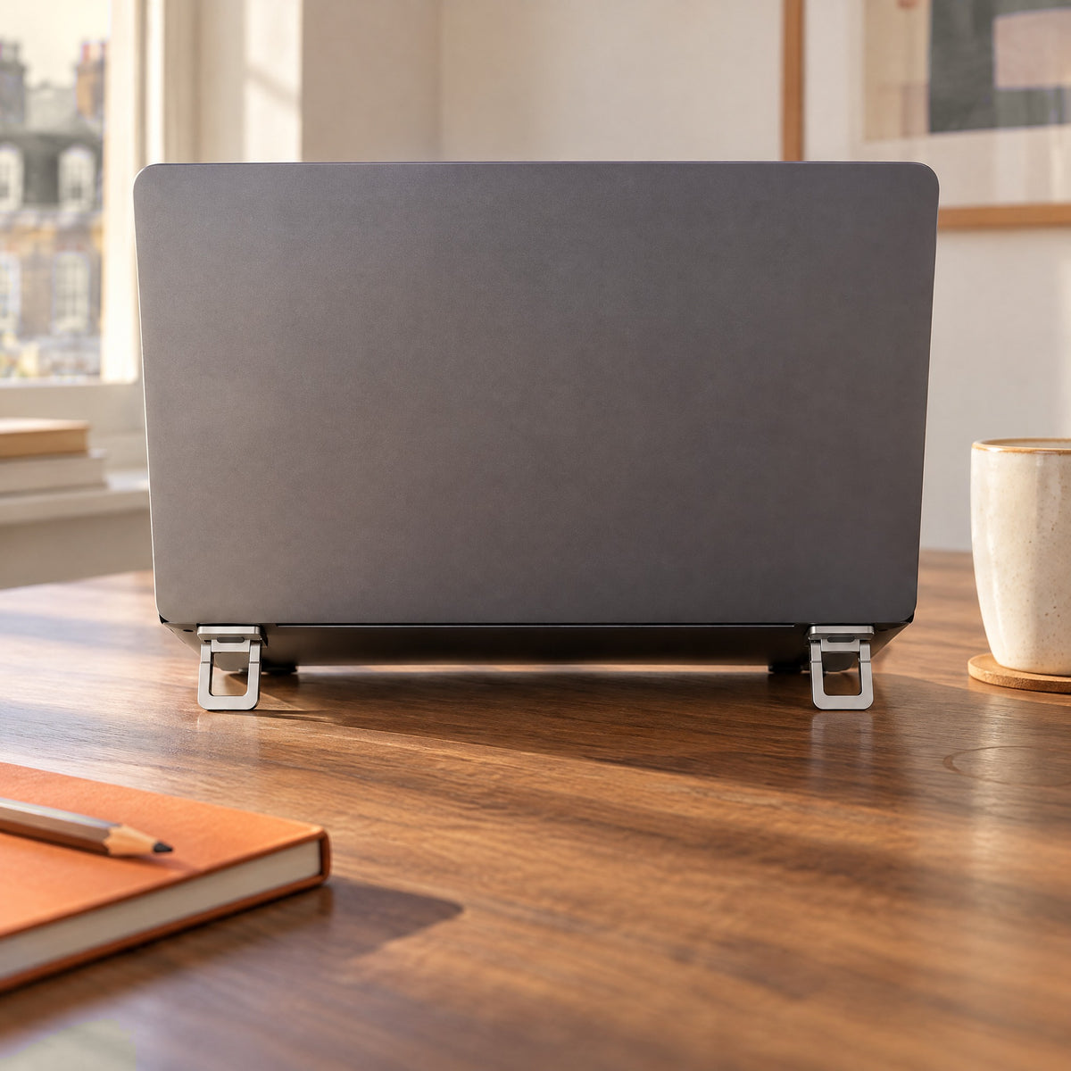 Back of a grey laptop raised on two silver Stilt feet on a walnut desk