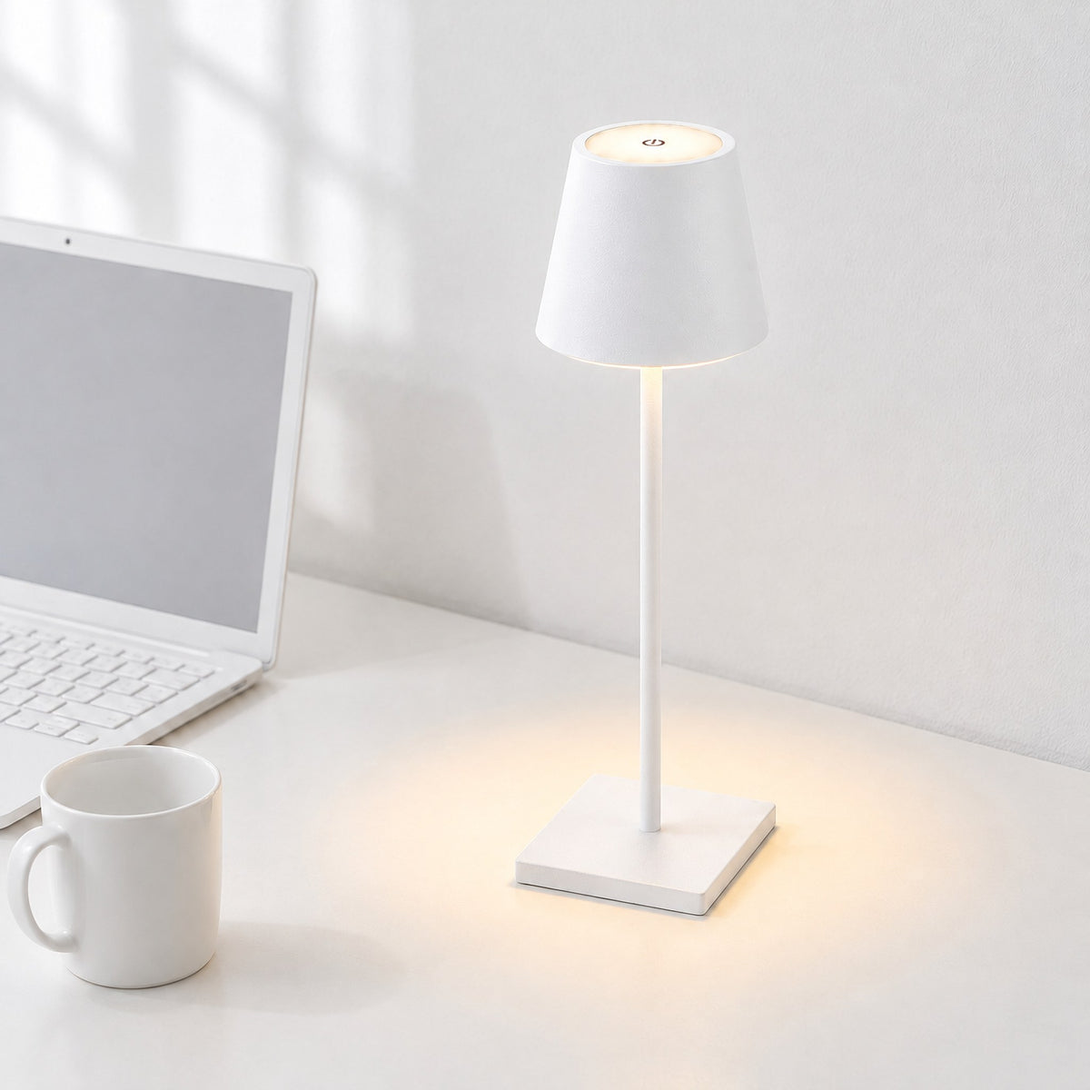 Vesper cordless LED table lamp in white, switched on, on a white desk beside a laptop and a white mug