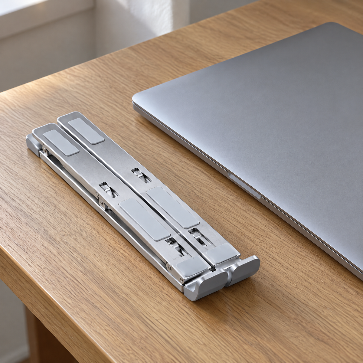 Tall laptop stand folded flat into a slim aluminium bar beside a closed laptop