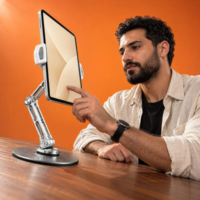 Man tapping a tablet held at eye level in the tablet holder of the Reach stand on a walnut desk