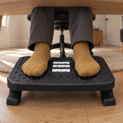 Feet in mustard socks resting on the Ease footrest under a desk, seen from the floor