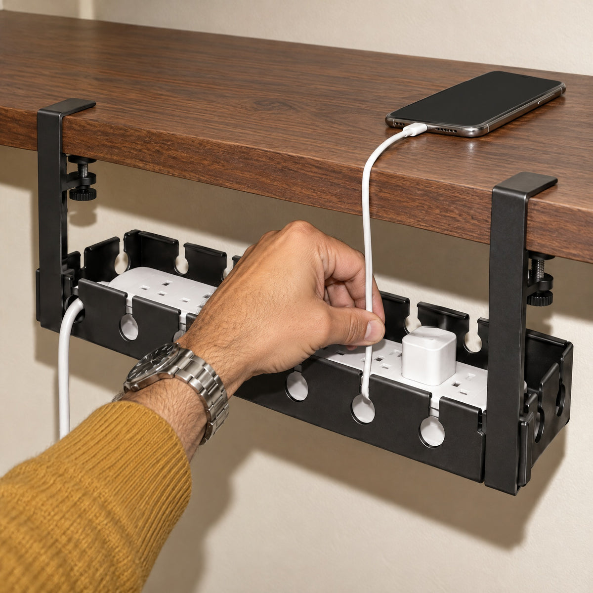 Hand pressing a phone cable into a slot of the black Hideaway under-desk cable tray