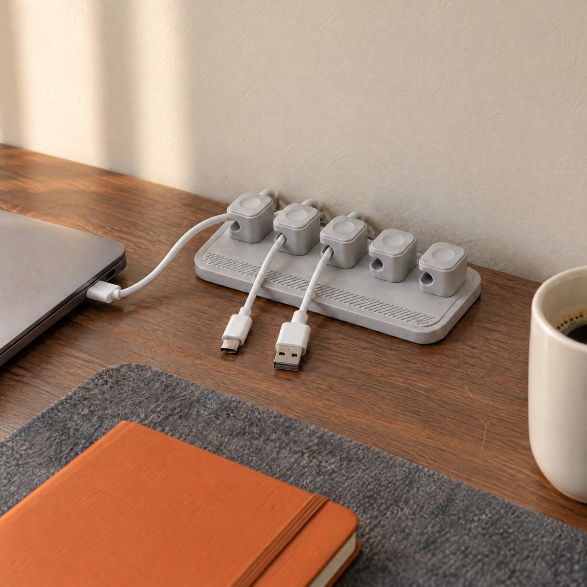 Grey magnetic cable holder on a walnut desk, one cable charging a laptop and two waiting in their clips