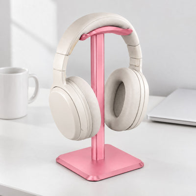 Perch headphone stand in pink holding cream headphones on a white desk