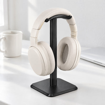 Black aluminium headphone stand holding off-white headphones on a white desk