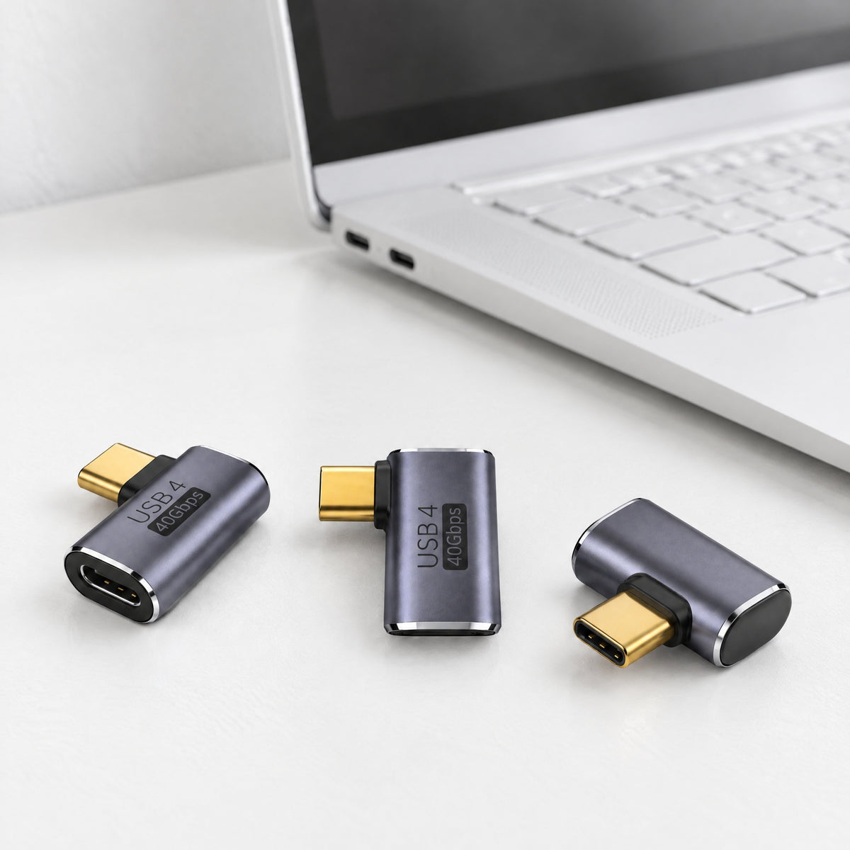 Three Elbow Side USB-C adapters in grey aluminium, plug leaving the side at a right angle, on a white desk beside a laptop