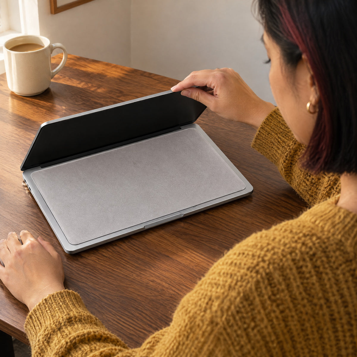 Woman lowering her laptop lid over a light grey microfibre cloth that covers the keyboard and trackpad