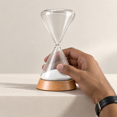 Hand reaching up to turn the Ebb hourglass over once the white sand has run through