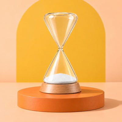 Ebb glass hourglass in its beech base on a low orange podium against a peach and yellow backdrop