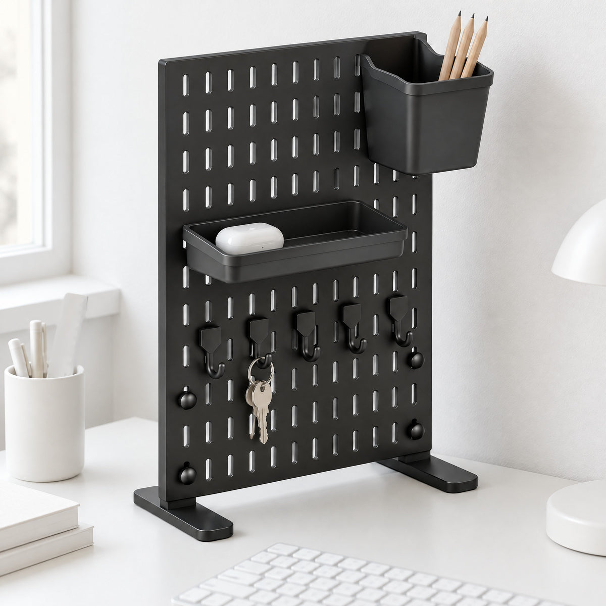 Black Trellis desk pegboard with a tray, a pencil bin and five hooks on a white desk behind a keyboard