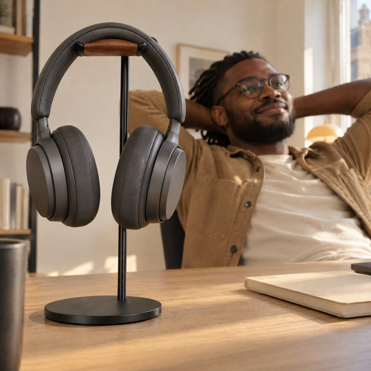 Man relaxing at his desk behind a black aluminium headphone stand holding dark grey headphones