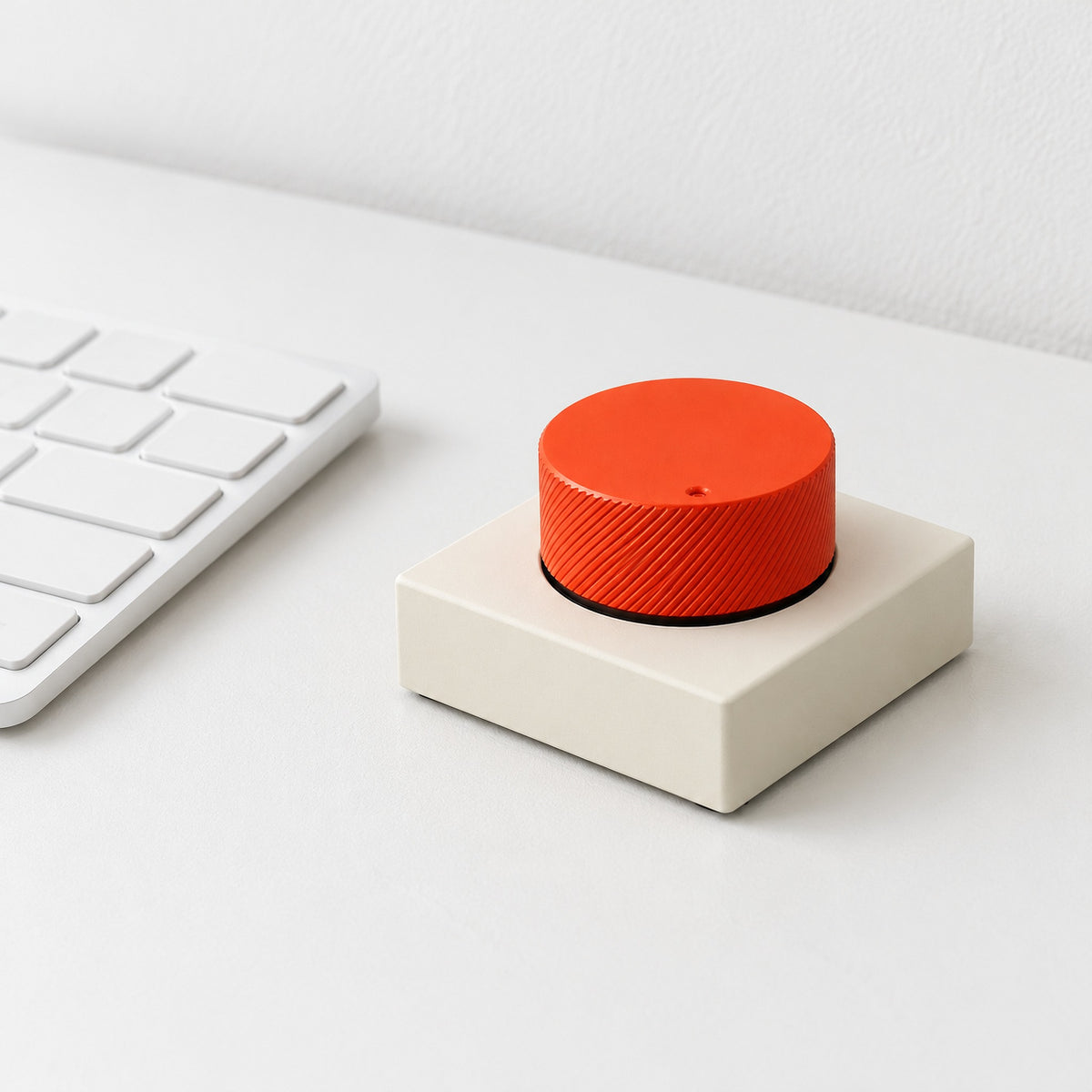 Capstan aluminium desktop control knob in cream and orange beside a white keyboard on a white desk