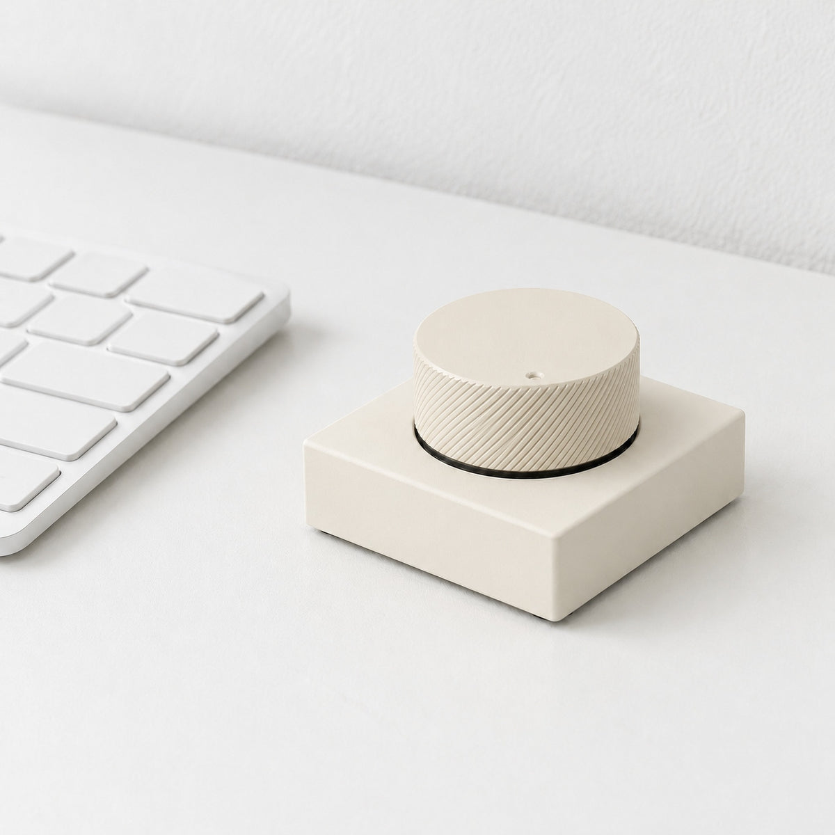 Capstan desktop control knob in cream, beside a white keyboard