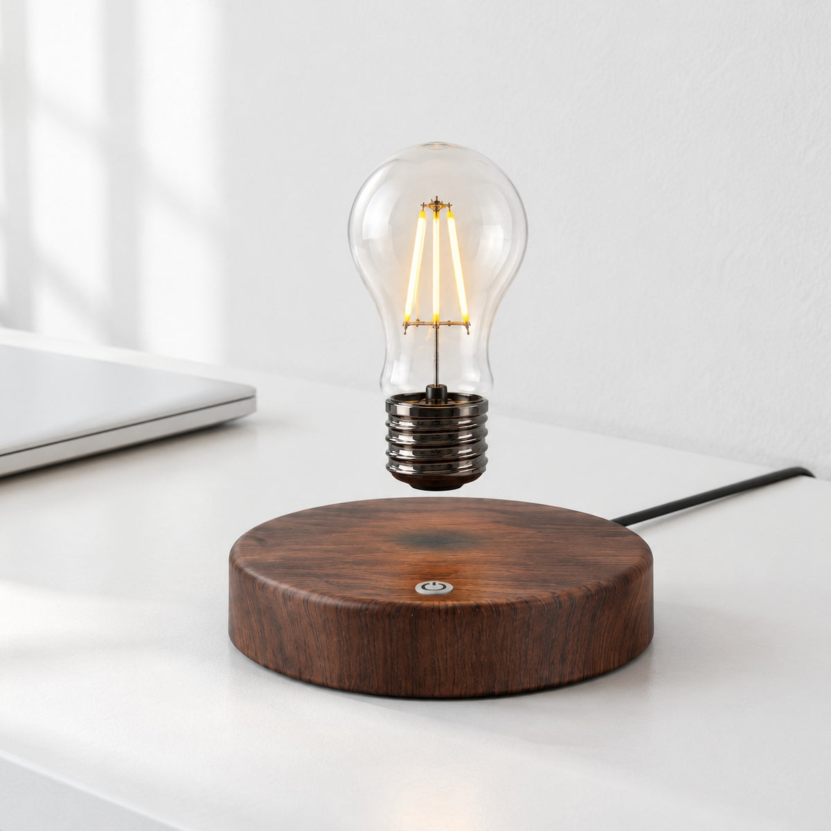 Drift levitating light bulb lamp with the round wood-grain base, lit, on a white desk