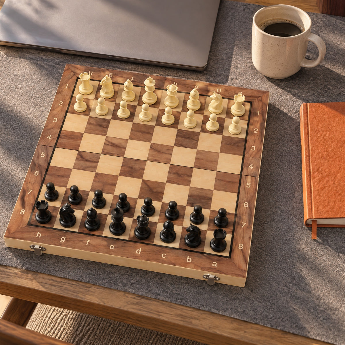 Gambit chess set ready for a game on a felt desk mat beside a laptop and a mug