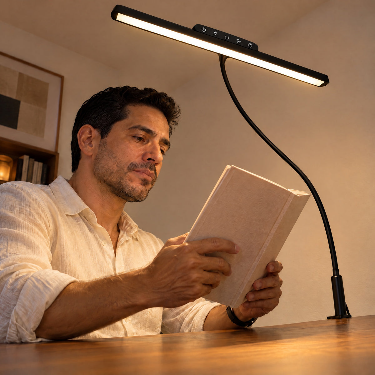 Man reading a book under the black Heron light bar clamped to his walnut desk in the evening