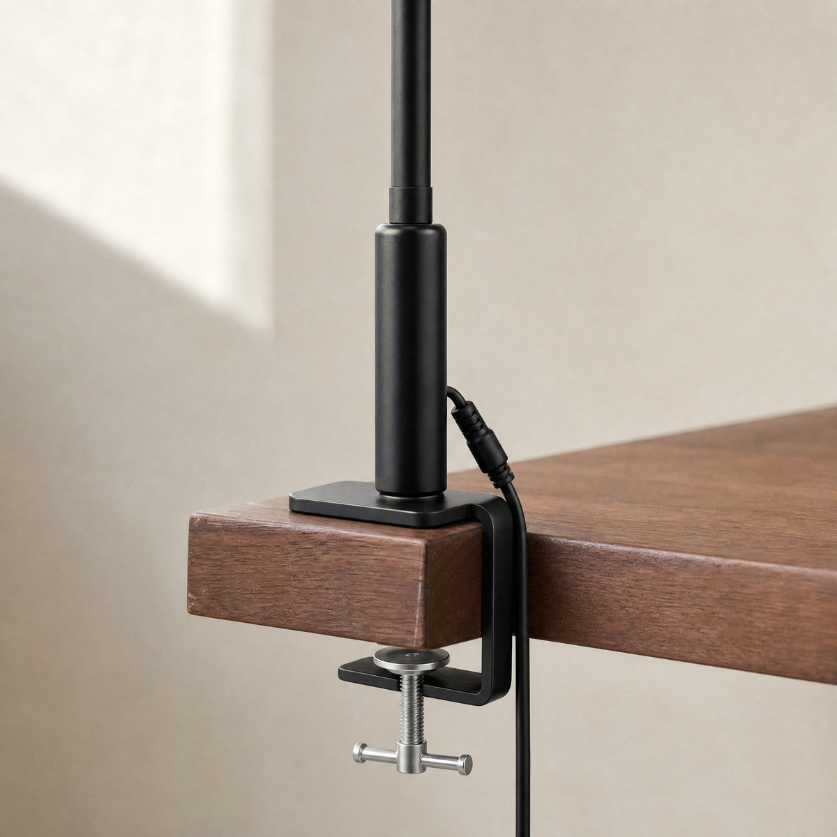 Black Heron desk lamp clamp gripping the back edge of a walnut desk, with its power cable