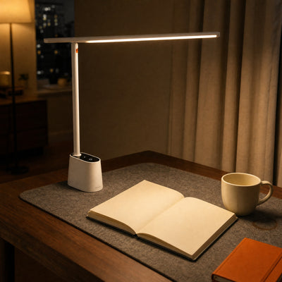 White Lintel desk lamp lighting an open book on a walnut desk in the evening