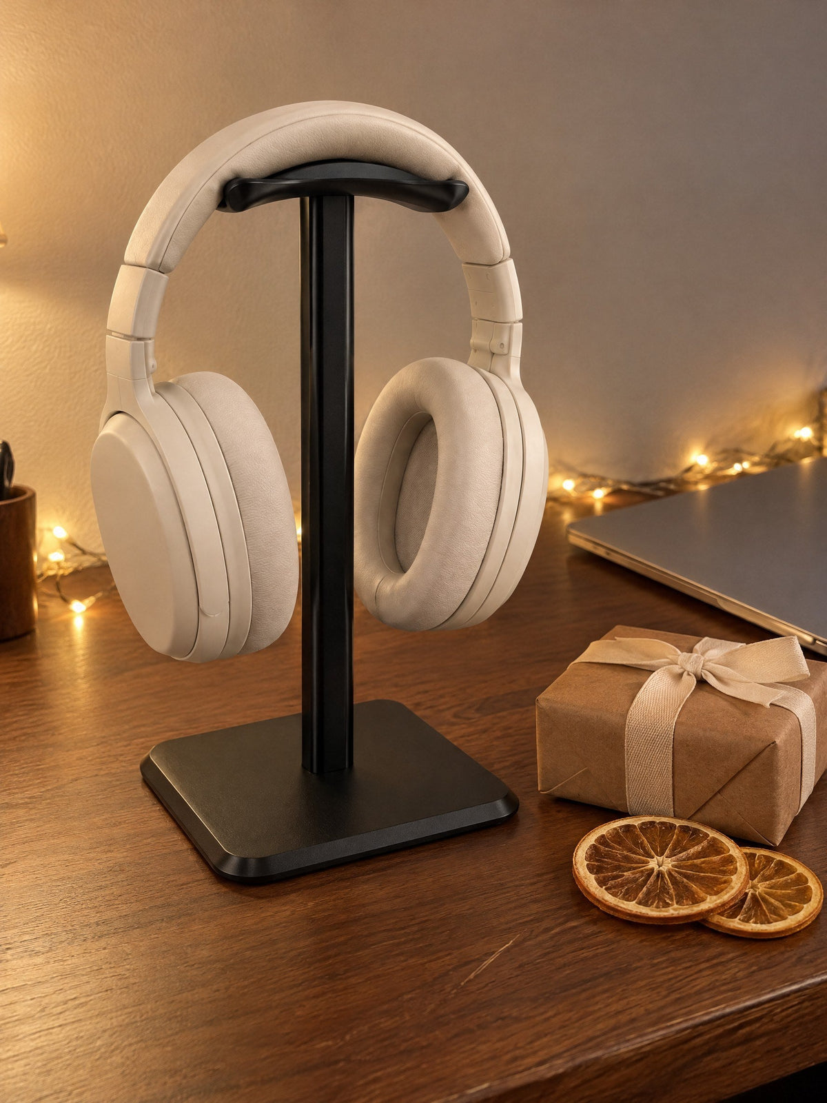 Black headphone stand holding cream headphones on a walnut desk with fairy lights and a small wrapped present