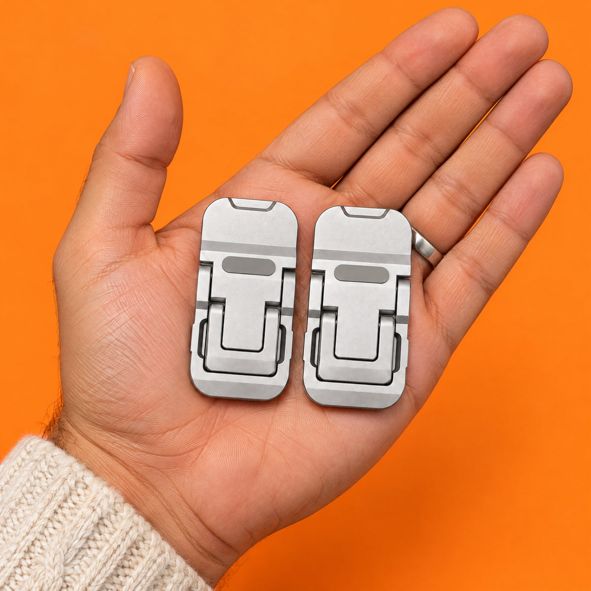 Two folded silver Stilt laptop feet on an open palm, shown at their real size