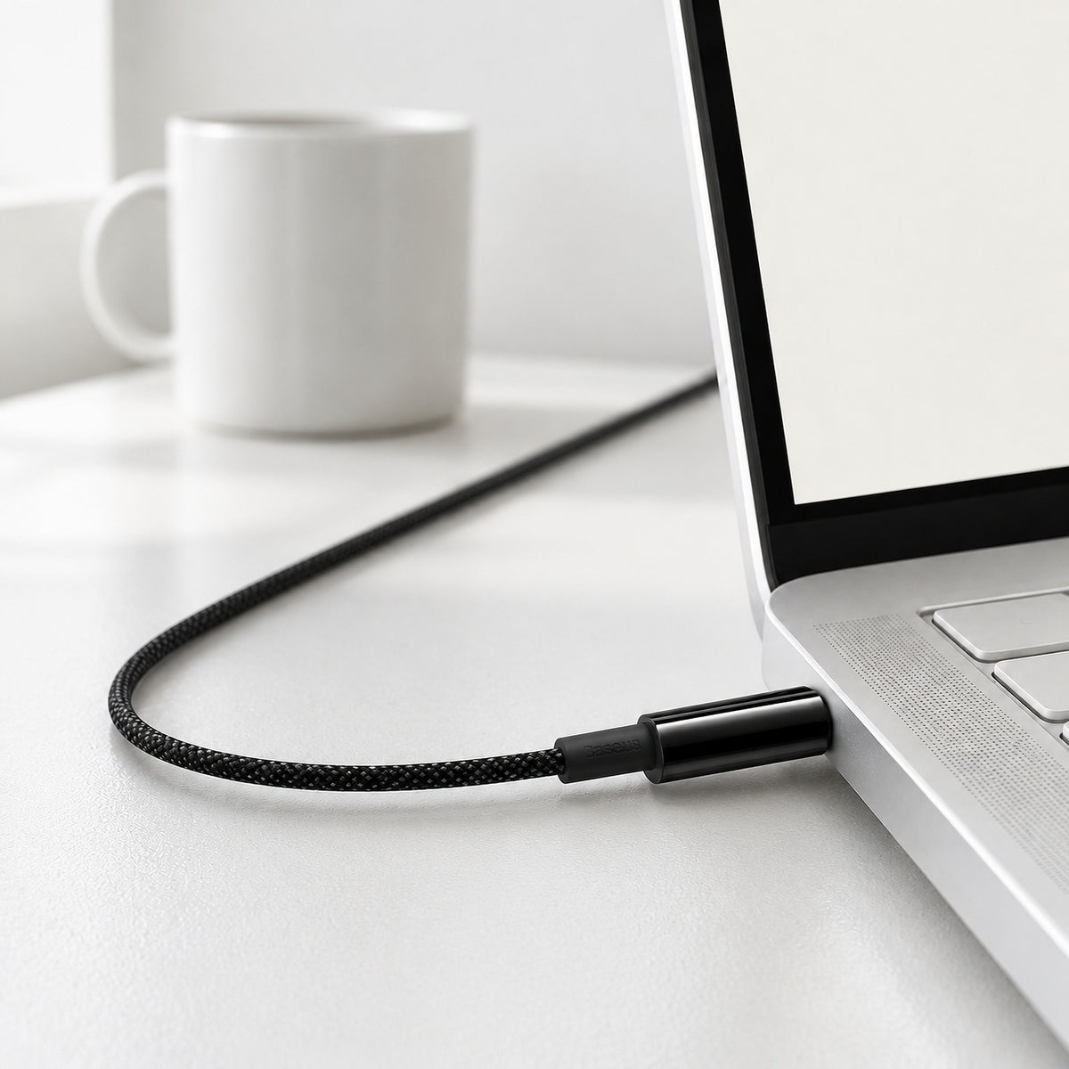 Black Strand braided USB-C cable plugged into the side of a white laptop on a white desk
