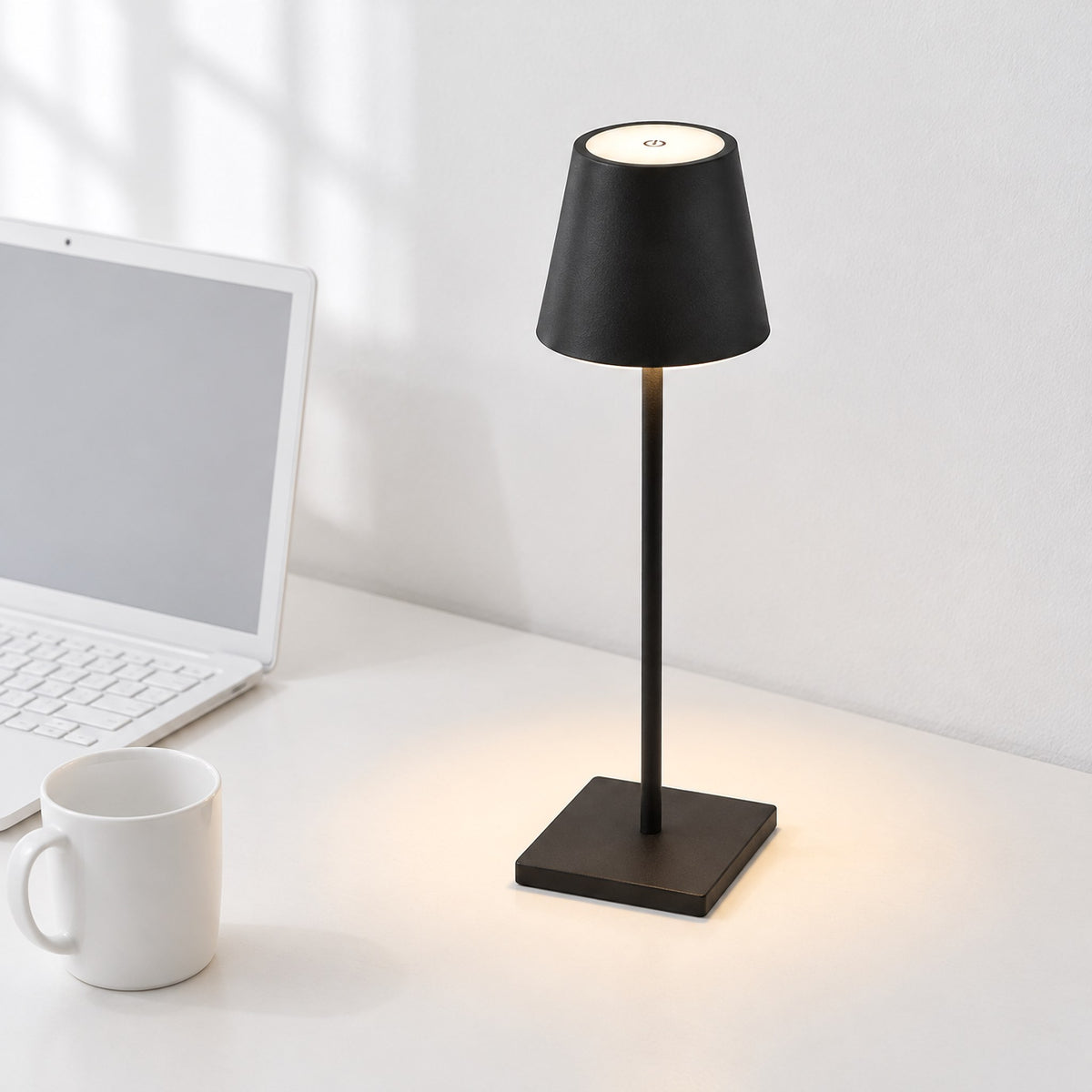 Vesper cordless LED table lamp in black, switched on, on a white desk beside a laptop and a white mug