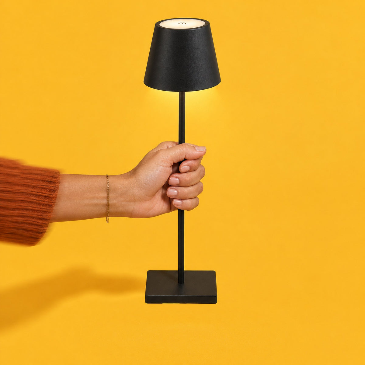 Hand carrying the switched-on black Vesper table lamp by its slim pole, no cable attached