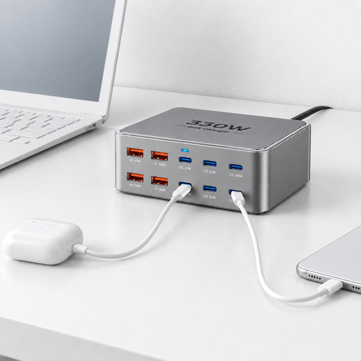 Grey Wharf 330W GaN charger on a white desk, charging earbuds and a phone by USB-C, black mains cable at the back